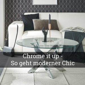 Modern eingerichtetes Wohnzimmer mit weißem Sofa, rundem Glastisch mit verchromtem Kreuzfuß, Kerzenhalter und dekorativer Handfigur; auf dem Bild steht der Schriftzug ‚Chrome it up – So geht moderner Chic‘.