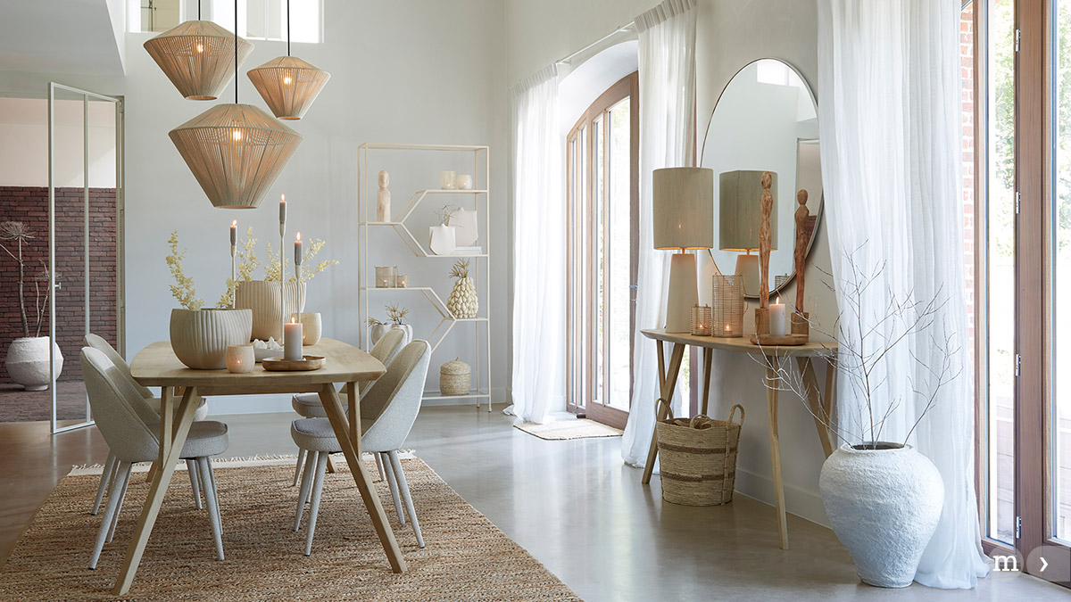 Heller Essbereich im natürlichen Wohnstil mit Holztisch, gepolsterten Stühlen, geflochtenen Pendelleuchten, dezenten Kerzen und dekorativen Vasen; große Fenster mit weißen Vorhängen sorgen für viel Tageslicht.